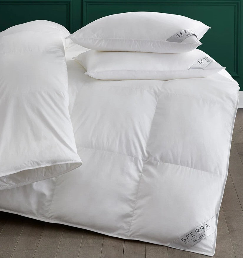 White bedding set with pillows on a bed, featuring the SFERRA brand.