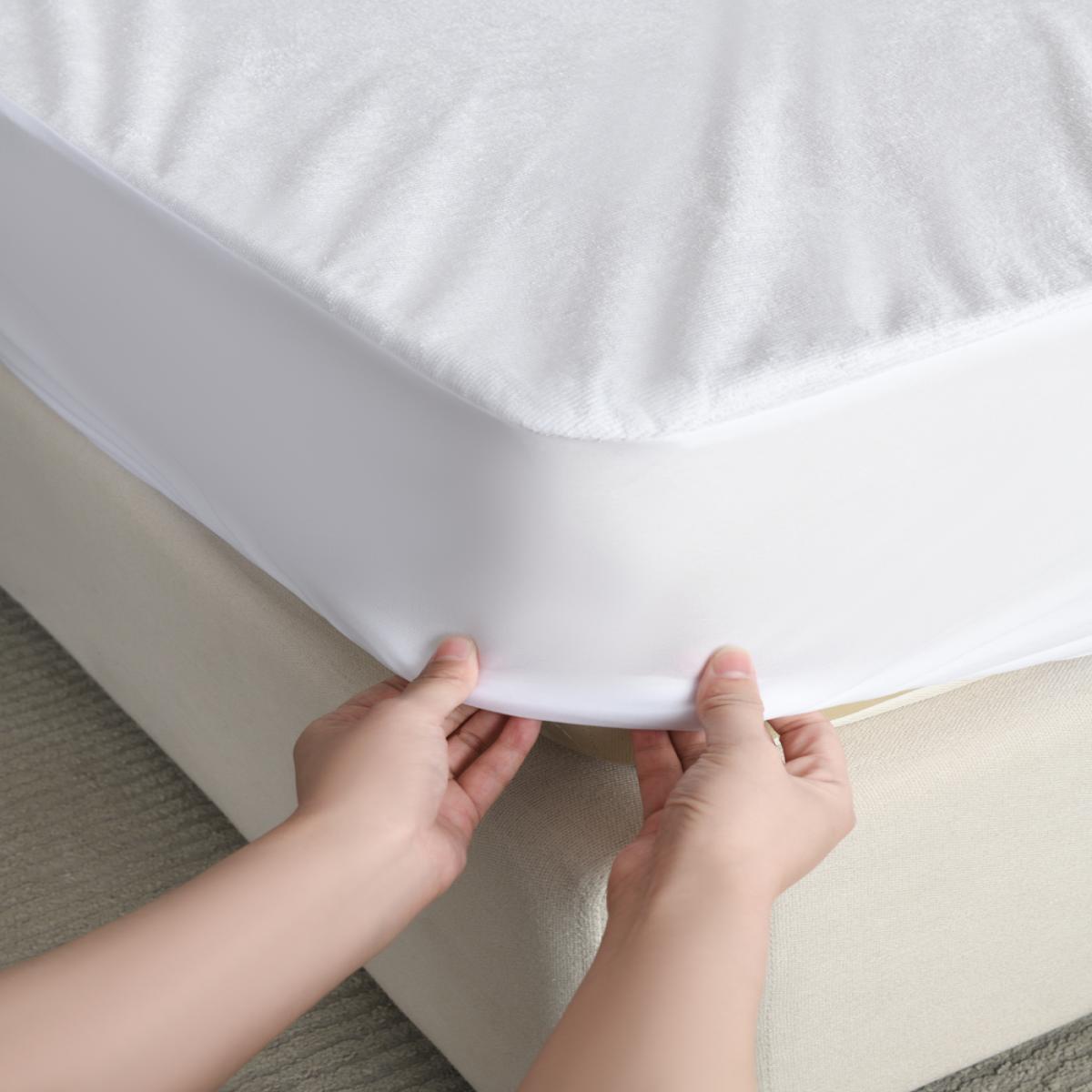 Person adjusting a white mattress protector on a bed. - Fitted sheet Design Bamboo Plus Mattress Protector.