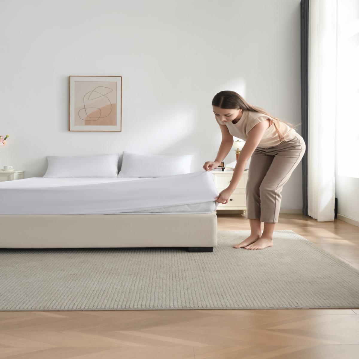 Woman preparing a bed with a mattress protector in a bedroom. - Bamboo Plus Mattress Protector
