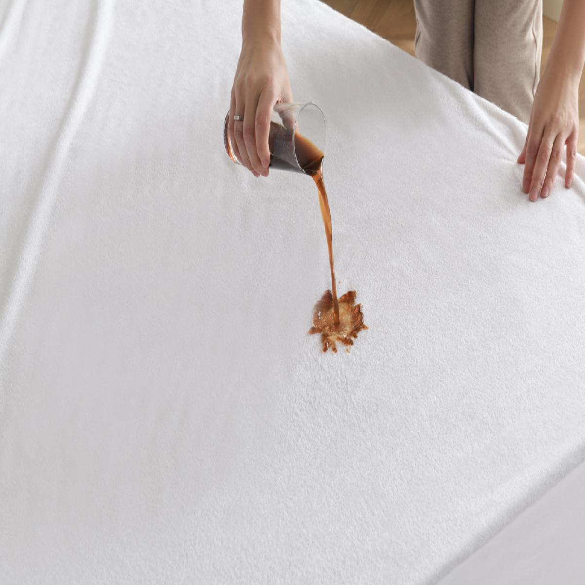Person pouring a brown liquid onto a white mattress - Bamboo Plus Waterproof Protection.